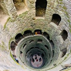 people are standing in the middle of a spiral staircase with stone walls and steps leading up to it