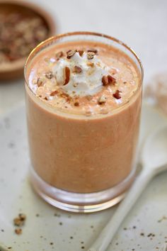 a smoothie with whipped cream and nuts in it on a plate next to a spoon