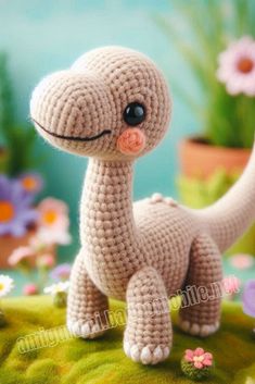 a small crocheted toy dinosaur sitting on top of a green surface with flowers in the background