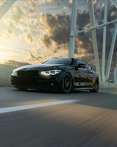 the black car is driving down the road in front of some tall white pillars and clouds