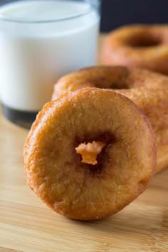 three doughnuts sitting on top of a wooden table next to a glass of milk