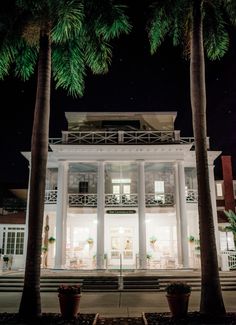 a large white house with palm trees in front of it and the lights on at night