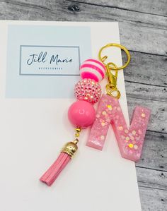 the letter w is made out of plastic and has pink beads, gold trimmings, and a tassel