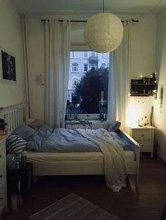 a bedroom with a bed, dresser and window in the room that has white curtains