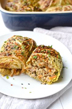 a white plate topped with cabbage covered in meat and veggies next to a casserole dish