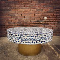 a round blue and white table sitting in front of a brick wall with a gold base