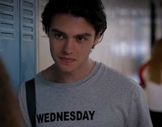 the young man is wearing a t - shirt that says wednesday on it, and he looks to his left