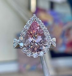 a pink diamond ring sitting on top of a wooden stick in front of a mirror