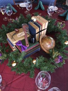 an arrangement of books and wine glasses on a red table cloth with christmas decorations around it