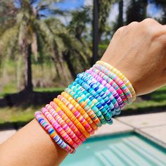 a person holding onto a stack of bracelets near a swimming pool with palm trees in the background