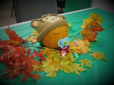 a stuffed animal sitting on top of a table next to autumn leaves and pumpkins