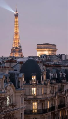 the eiffel tower is lit up at night, with buildings in the foreground