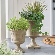 two cement planters with plants in them on the front porch, next to a door