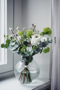 a vase with flowers and greenery on a window sill