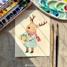 a drawing of a deer holding a gift in his hand next to paintbrushes and watercolors