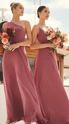 two women in long dresses standing next to each other with flowers on their heads and holding bouquets