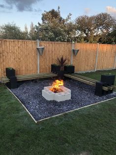 an outdoor fire pit in the middle of a yard with grass and wooden fence behind it