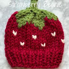 a red knitted strawberry hat with green leaves on top and the words strawberries beanie above it