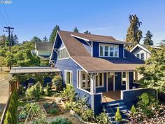 a blue house with lots of trees and plants in the front yard on a sunny day