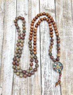 This beautiful Mala feels masculine and would make a great gift for a man.  You get a good feeling of being grounded to Mother Earth. 📿10mm genuine Sandalwood beads and 10mm Picture Jasper.   📿Guru Bead is Brass Tibetan bead inlaid with red coral and turquoise.  About 30mm with OM design in center. 📿4 bronze hematite spacers at marker 7 and 21 each side of the Guru 📿Hand-knotted on Nylon Red thread between the semi-precious gemstones only, 📿The Mala is finished off with tiny gold color hematite beads and 6mm sandalwood beads. 📿It is approximately 25" 📿 Picture Jasper is a nurturing, protective stone, It brings comfort and alleviates fear, stimulating not only the Base Chakra in providing physical and spiritual energy for the body, but also activates the Third Eye Chakra enhancing vi Earthy Wooden Beads As A Gift, Bohemian Brown Mala As Gift, Bohemian Style Brown Mala For Gift, Bohemian Style Brown Mala As Gift, Artisan Brown Beaded Necklaces With 8mm Beads, Rustic Round Beads Jewelry For Meditation, Rustic Jewelry With Round Beads For Meditation, Rustic Round Bead Jewelry For Meditation, Rustic Brown Jewelry With 8mm Beads