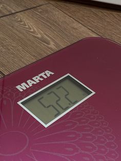 a digital bathroom scale with the time displayed on it's display panel and wood flooring