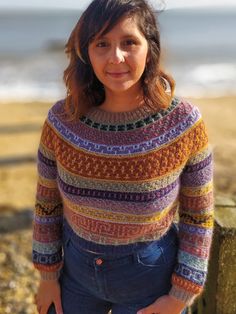 a woman is standing on the beach with her hands in her pockets and looking at the camera