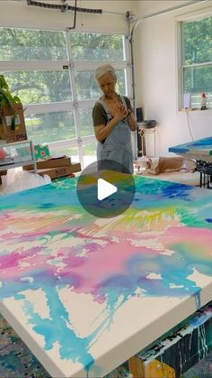 an older woman standing in front of a large table covered in colorful paint and holding a microphone