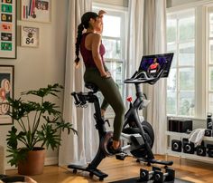 a woman is riding an exercise bike in the living room while looking at her laptop