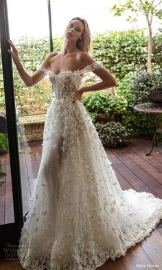 a woman in a white wedding dress standing by a glass door with her hands on her hips