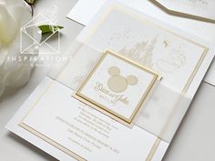 a white and gold wedding card with a mickey mouse on the front is next to a flower