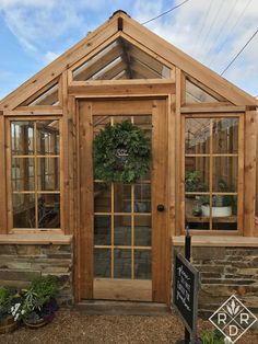 a small wooden greenhouse with glass doors and windows on the outside, in front of a stone wall