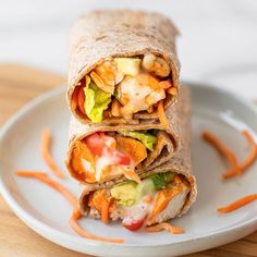 a chicken caesar wrap on a plate with carrots and lettuce in it