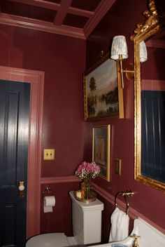 a white toilet sitting next to a bathroom sink under a framed painting on the wall