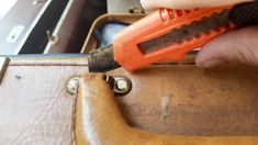 a person holding an orange and black tool in their hand next to a piece of luggage