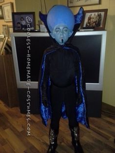 a man dressed in blue and black is standing next to a television screen with an evil mask on it's head