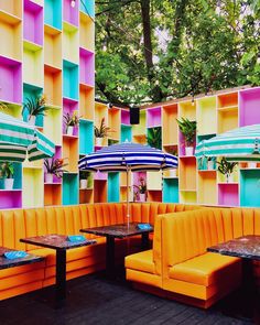 an outdoor seating area with tables and umbrellas in front of multicolored walls