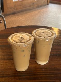 two drinks sitting on top of a wooden table next to each other in plastic cups