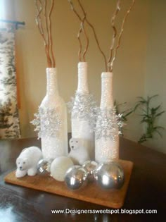 three white vases with silver balls and branches in them sitting on a wooden tray