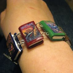 two bracelets that have books attached to them on someone's arm, one with a book and the other has a lighter in it