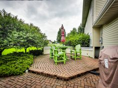 there is a patio with green chairs and a table on the brick floor next to some bushes