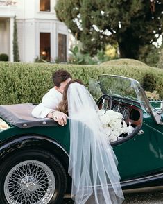 a bride and groom kissing in an old fashioned green convertible car with white flowers on the front