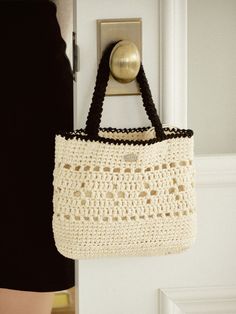 a crocheted purse hanging on a door handle next to a woman's black dress