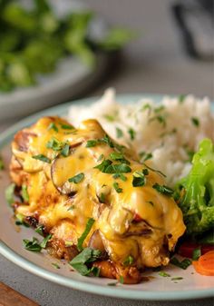 a white plate topped with meat covered in cheese next to rice and veggies