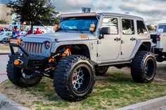 a gray jeep parked on top of a lush green field next to a parking lot