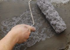 a hand is holding a paintbrush near a large piece of cement on the ground