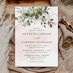 an elegant wedding card with watercolor flowers and greenery is displayed on top of a furnishing