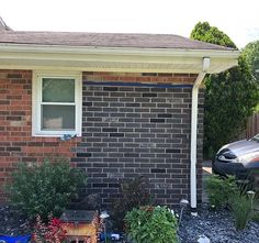 a car parked in front of a brick house with plants growing out of the driveway