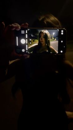 a woman holding up a cell phone to take a photo with her self in the dark