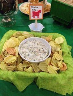 a bowl of dip surrounded by chips and crackers on a green table cloth with a sign that says potato field