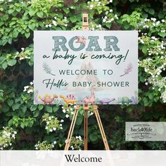 a welcome sign for a baby shower is displayed in front of some flowers and greenery